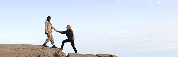Two women on a cliff next to ocean, holding hands.