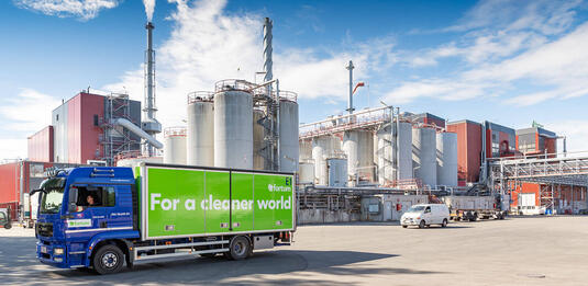 A green and blue truck with Fortum's tagline For a cleaner world leaving the waste-to-energy plant yard.