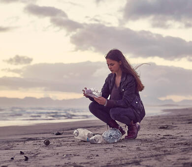 A woman at a beach is holding plastic waste in her hands.